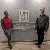 Tracey Karuhogo and Robert Daudet stand by the University of Manitoba Student Union sign.
