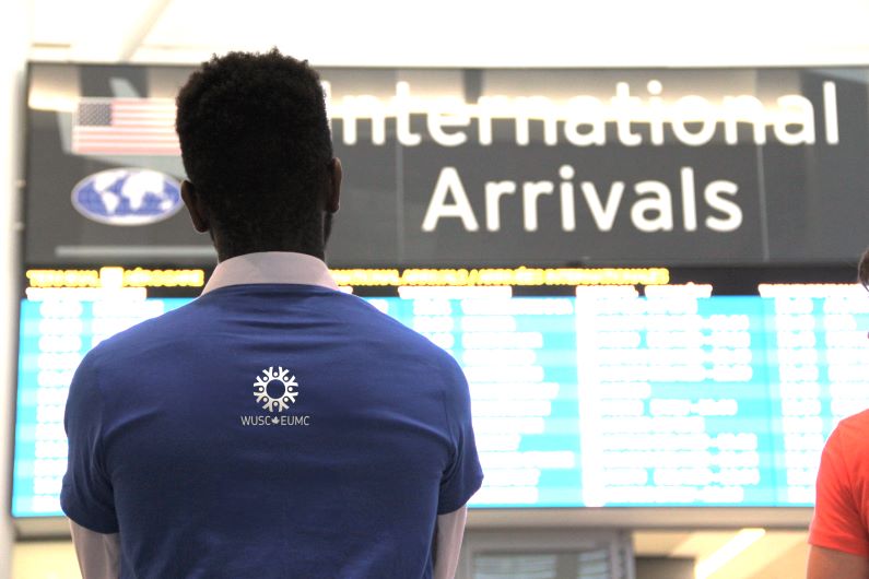 WUSC volunteer looks at the arrivals screen at Toronto Pearson International Airport