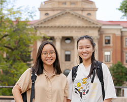 Two female students smiling in front of university building