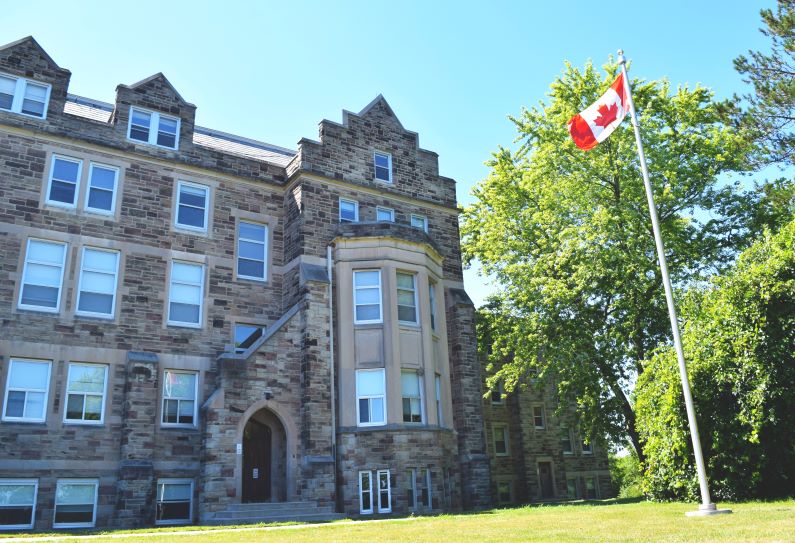 Image of a stone building and Canadian flag on the campus of Western University